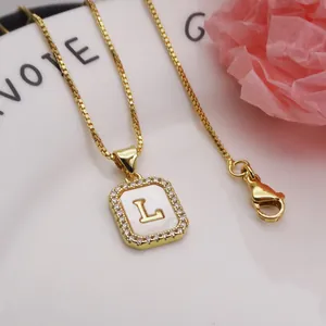 Close-up of square gold pendant necklace with shell inlay and letter L detail
