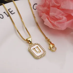Close-up of a gold square pendant necklace featuring a shell-inlaid letter U