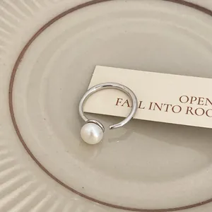 Primo piano di un anello aperto in argento con una perla bianca lucida e raffinata.