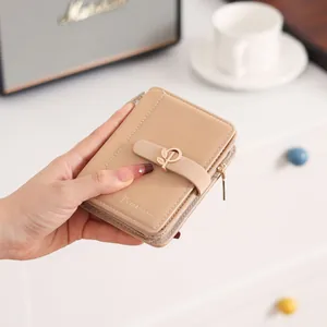 Close-up of apricot PU leather short wallet with decorative leaf buckle held in hand
