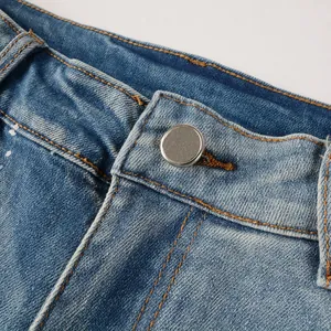 Close-up of denim jeans waistband with metal button and white paint splatters.