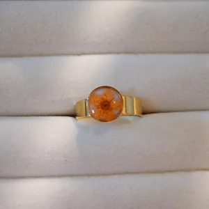 Nahaufnahme eines goldenen Edelstahlrings mit einer echten orangefarbenen Trockenblume