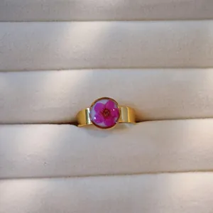 Nahaufnahme eines goldfarbenen Edelstahlrings mit echter rosa Trockenblume in Harz