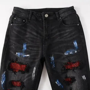Detailansicht schwarze Jeans mit roten Strasssteinen und blau-weißen Farbspritzern.