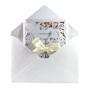 Elegante invitación de boda cortada con láser con sobre blanco y lazo de raso crema.