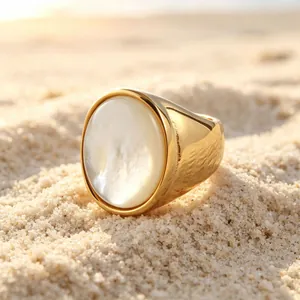 Vergulde roestvrijstalen zegelring met een witte parelmoer inleg op het zandstrand