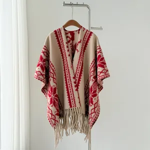 Ethnic style beige knitted poncho with red patterns and tassels on a clothes hanger