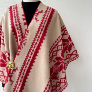 Detailed view of beige and red ethnic style poncho featuring tribal patterns and gold brooch