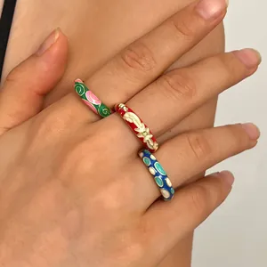 Close-up of colorful retro enamel rings on fingers with floral and geometric patterns.