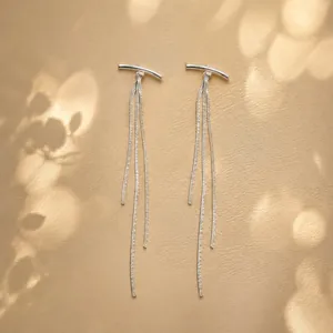 Detail view of elegant silver-colored long chain tassel earrings on a textured surface.