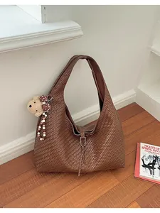 Gedetailleerde weergave van bruine hobo-tas met weeftextuur en schattige berenhanger