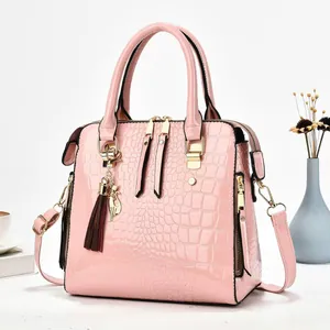 Elegant pink patent leather handbag with crocodile texture and decorative cat charm.