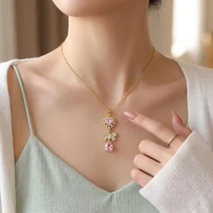 Close-up detail of a delicate gold necklace with a pink heart and waterdrop stone pendant