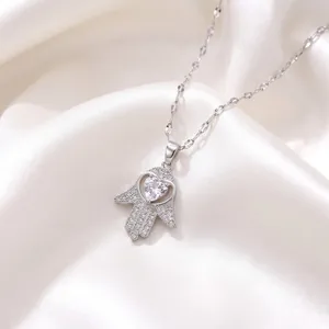Detailed close-up of a silver Hamsa hand necklace pendant featuring a sparkling heart-shaped zircon.