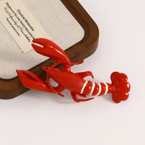 Detailed view of a glossy red lobster brooch with white stripes on a jewelry tray