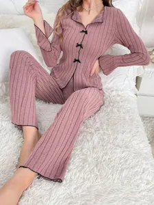 Close-up of model wearing pink ribbed pajama set with bows and wavy trim on soft rug