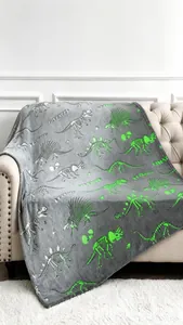 Detalle de la manta de franela gris que brilla en la oscuridad con esqueletos de dinosaurio