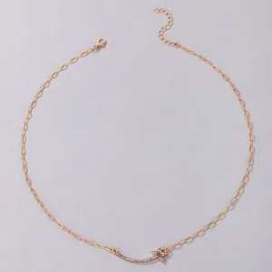 Close-up of gold chain necklace with rhinestone curved bar and small cross pendant