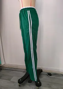 Side view of green wide-leg athletic pants featuring double white stripes and drawstring