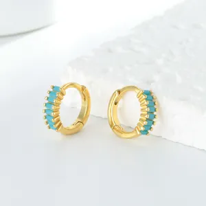 Détail de boucles d'oreilles créoles dorées avec incrustations turquoise sur pierre