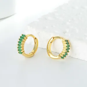 Gros plan de boucles d'oreilles créoles dorées avec zircons verts en taille baguette de détail