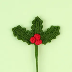 Detailed view of hand-knitted crochet holly branch with red berries for Christmas decor.
