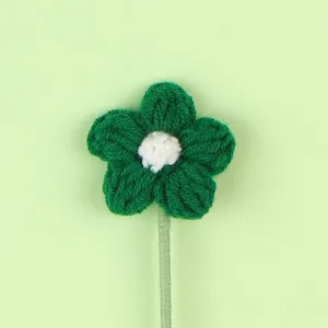 Macro detail of a handmade green crochet knitted flower with a white center on a stem