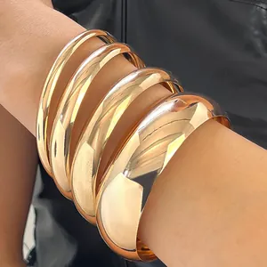 Macro view of wide gold alloy bangles stacked on wrist with high glossy finish