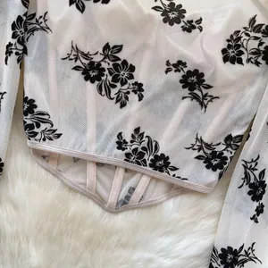 Detailansicht eines transparenten Mesh-Oberteils mit schwarzen floralen Flockdruck-Details