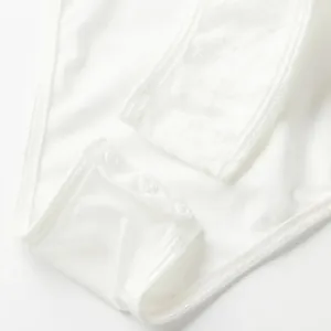 Macro view showing the high-quality snap button closure and lace texture of the white bodysuit