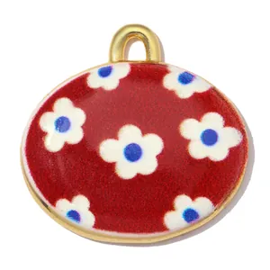 Makro-Detail eines roten Emaille-Ovals mit weißen Blumenmustern und vergoldeter Schlaufe.