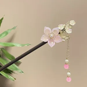 Close-up of a traditional sandalwood hair stick with pink floral accents and bead tassels.