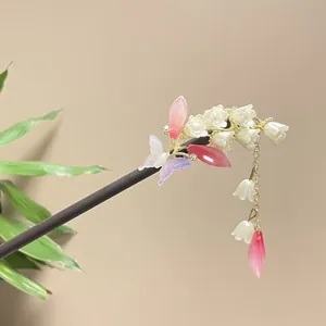 Detail view of a handcrafted wooden hairpin with lily of the valley and silk tassel.