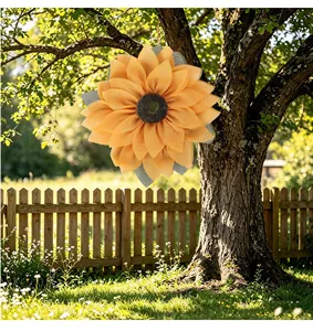 Large orange fabric sunflower wreath decoration hanging on a tree trunk in a sunny garden setting