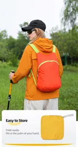 Macro detail view of a lightweight orange foldable hiking backpack shown in use outdoors.