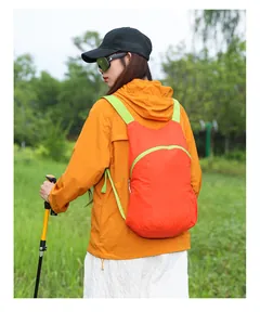 Detail view of a lightweight orange hiking backpack worn by a hiker in a nature setting