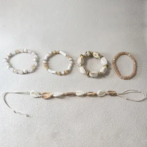 Vista detallada del juego de pulseras bohemias en crema y oro con dijes de conchas