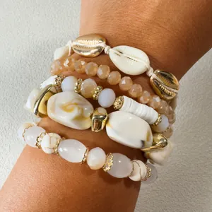 Primer plano de pulseras de cuentas bohemias con dijes de caracoles dorados y blancos