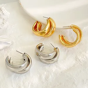 Detailed close-up of chunky gold and silver layered hoop earrings on white stone texture