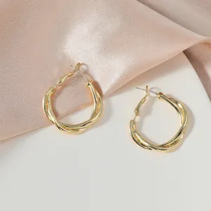 Elegant gold twisted hoop earrings displayed on soft pink satin and white surface