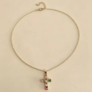 Dettaglio macro di un'elegante collana d'oro con pendente a croce in cristallo multicolore