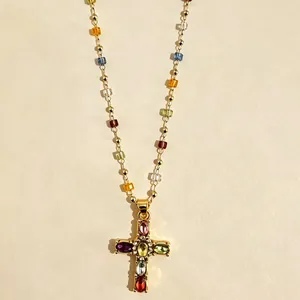 Dettaglio di una collana con ciondolo a croce dorata, cristalli colorati e perline fini.