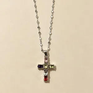 Dettaglio macro di un ciondolo a croce in argento con cristalli multicolore brillanti.