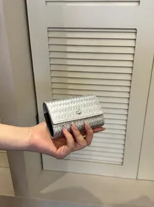Primo piano di una mano che tiene una elegante borsa a mano intrecciata argento da donna