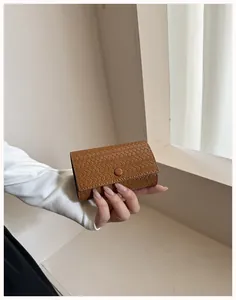 Dettaglio della texture intrecciata di questa pochette in pelle marrone tenuta in mano