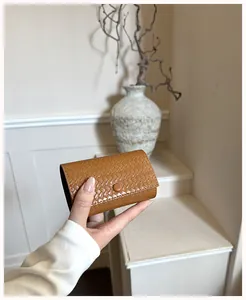 Portacarte in pelle intrecciata marrone tenuto a mano in un interno crema minimalista.