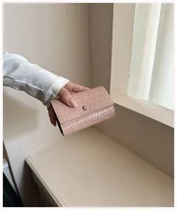 Primo piano di un portafoglio intrecciato rosa cipria con chiusura a scatto nella mano.