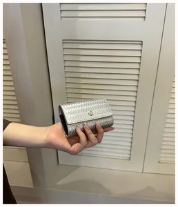 Dettaglio di un elegante portafoglio intrecciato argento da donna tenuto in mano.
