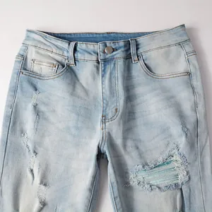Close-up detail of light blue distressed denim jeans with ripped knee and waistline