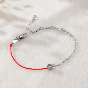 Nahaufnahme eines Glücks-Armbandes mit roter Schnur, Zirkonia und Silberkette.